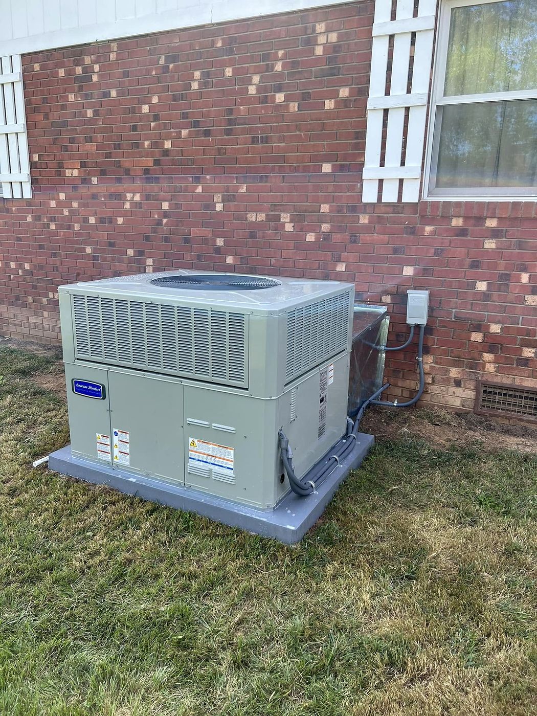 New packaged heating and cooling unit installed on a pad beside a brick home